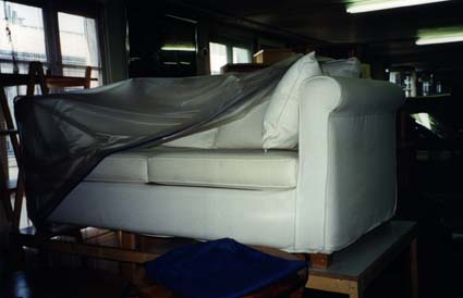  Canapé blanc recouvert de moitié d'une bâche plastique grise.