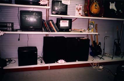  Rayonnage de magasin avec téléviseurs, enceintes et guitares électriques.