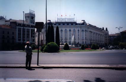  Homme debout face à un poteau devant un rond-point avec bosquets et fontaines.
