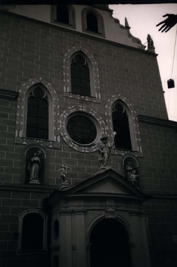  Façade d'église avec fenêtres en ogive et une main en avant-plan. Noir et blanc.