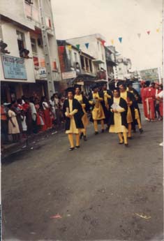  Défilé d'hommes en habit noirs et jaunes dans une rue passante.