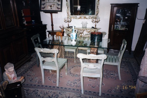 Table en verre avec bibelots et cinq chaises à dossier ouvragé.