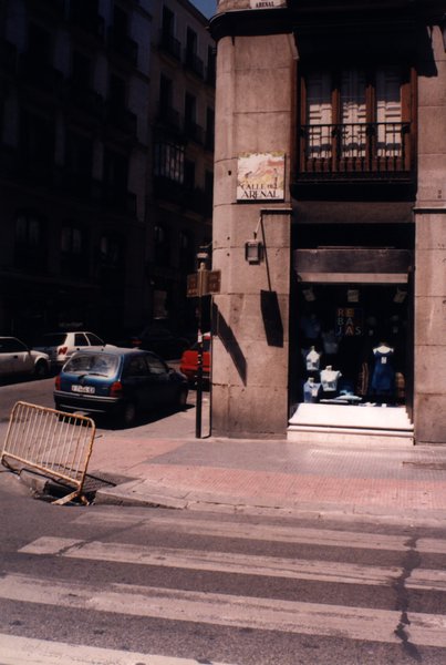 Coin de rue avec plaque « Calle del Arenal » et vitrine de magasin.ᴬᴵ
