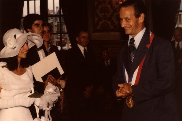 Mariée souriant à un homme portant l'écharpe tricolore, à l'intérieur d'une mairie.ᴬᴵ